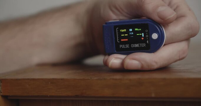 Home patient activates a pulse oximeter and views its digital readout, illustrating oxygen saturation measurement and personal health monitoring.