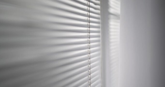 A window with blinds is shown in a close up. The blinds are white and the window is partially covered