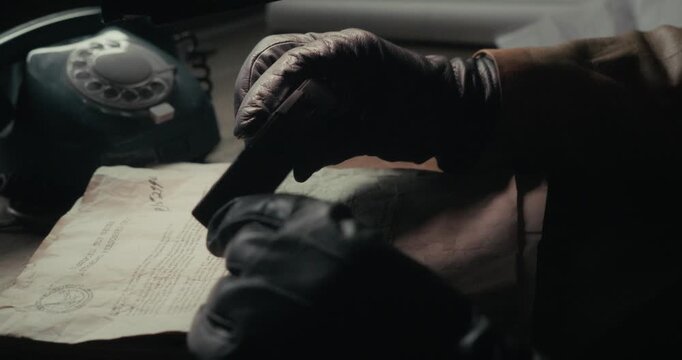 Gloved hand uses a miniature camera to photograph documents in dark shadows, evoking clandestine surveillance, undercover intelligence and vintage spy drama.