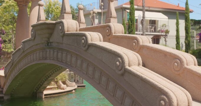 Ornate stone bridge arches over pond in Villa Grock gardens, Italian Riviera setting
