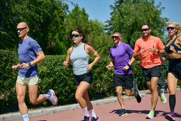 Obraz premium Close side view of diverse runners training together in bright summer sunlight. Concept of performance training, athletic lifestyle and shared progress.