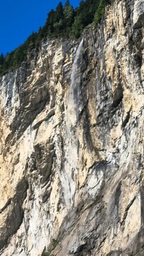 Parete rocciosa con cascata sottile e alberi sotto cielo limpido