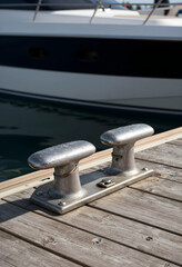 Fototapeta premium Maritime travel and luxury yachting lifestyle, metal mooring cleat on a wooden pier with a docked boat in a marina harbor for nautical vacation