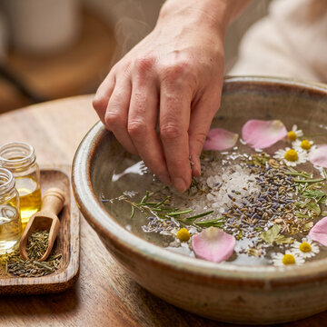 Woman preparing a relaxing herbal facial steam with sea salt, lavender, chamomile, and rose petals in a ceramic bowl
