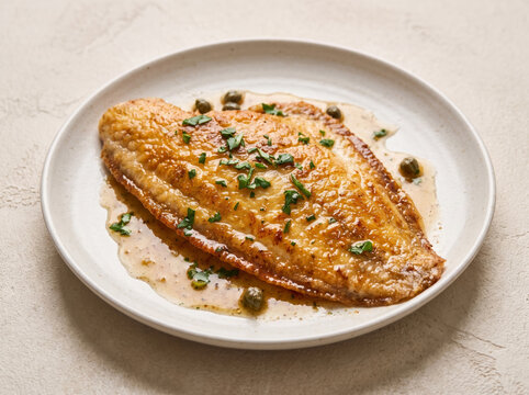 Pan seared sole meuniere fish fillet in lemon butter caper sauce on a ceramic plate