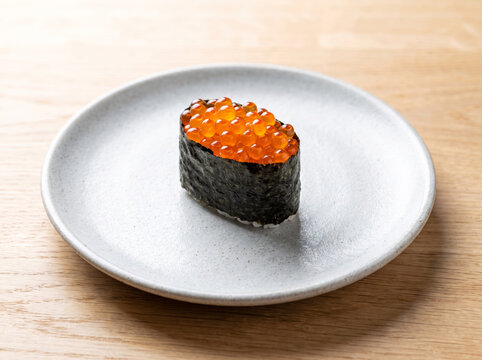 Single fresh ikura salmon roe gunkan sushi on a round ceramic plate