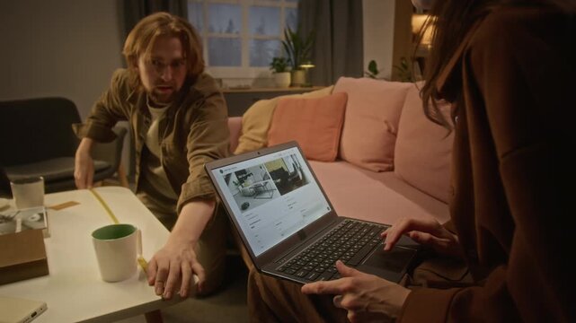 Young Caucasian woman browsing furniture website on laptop while Caucasian man measuring with tape measure. Video ideal for e-commerce advertising and interior design campaigns
