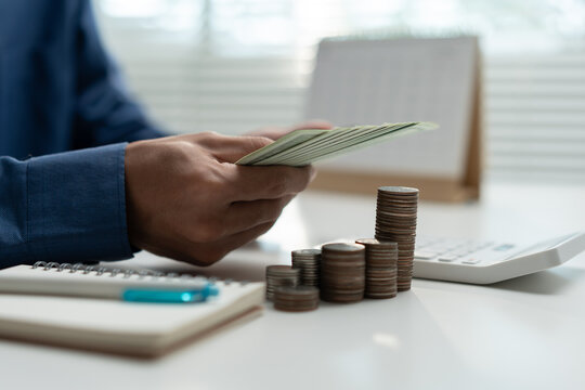 Close-up of a person counting cash beside stacked coins, calculator and notebook, representing financial planning, budgeting, savings, investment growth, money management and business finance.