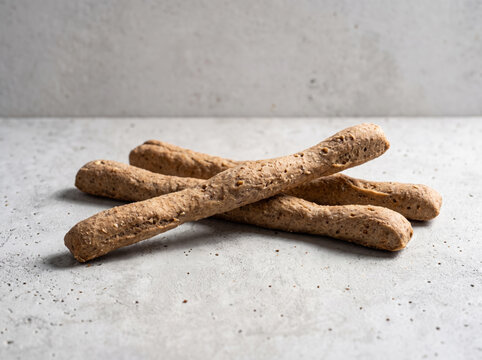 Whole grain rye grissini breadsticks stacked on a light textured surface