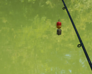Fishing bobber hangs on fishing line above calm water in a serene area at midday during warm weather with green reflections visible in the water surface © Miroslav