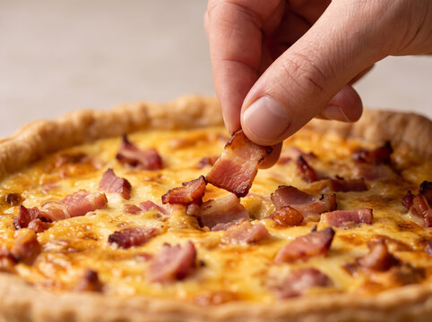 Hand picking a crispy bacon bite from freshly baked quiche lorraine