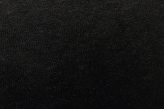 Macro close-up of a black grainy textured surface background,A detailed macro photograph of a dark, black surface with a distinct, fine, granular and pebbled texture. The surface has a matte finish.
