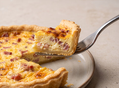 Fork lifting slice of freshly baked quiche lorraine with bacon and cheese