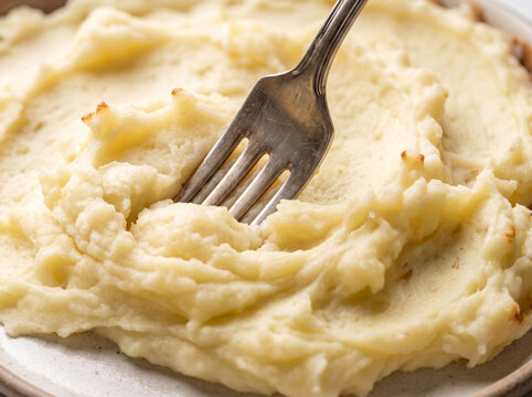 Fork making textured pattern in creamy buttery mashed potatoes