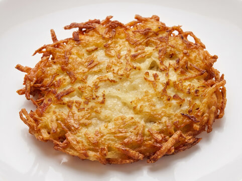 Golden crispy potato rosti pancake served on a white ceramic plate