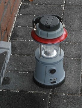 Lantern placed on a gray pavement beside a brick wall in a well-lit area