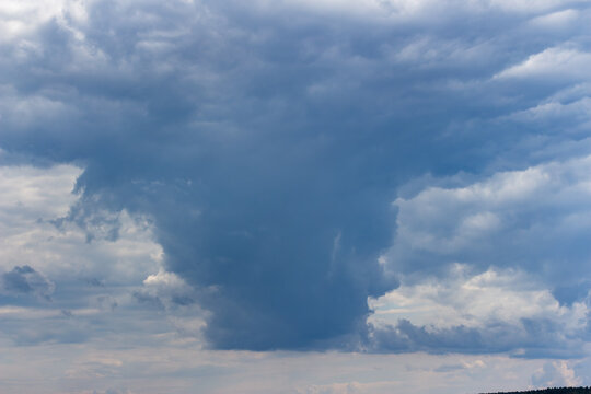 Massive dark cumulus storm cloud dominating a moody overcast sky, dramatic atmospheric textures with heavy rain-laden vapors gathering before an impending downpour in a wide open sky