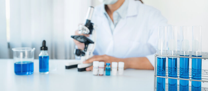 Scientist woman in medical face mask using microscope and test t