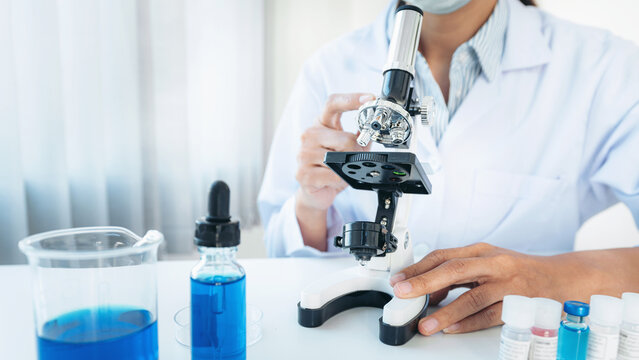 Scientist woman in medical face mask using microscope and soluti
