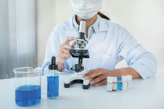 Scientist woman in medical face mask using microscope and soluti