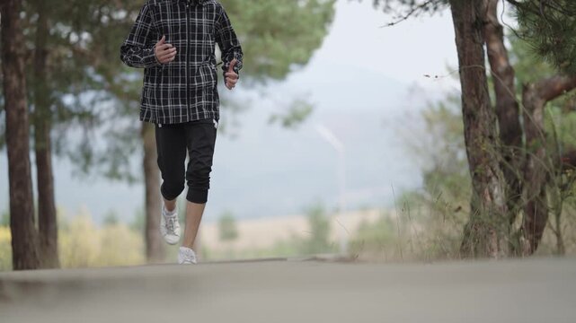 A man is running, jogging in a forest with a plaid jacket. The man is wearing white shoes and a black jacket, isolated cinematic shot