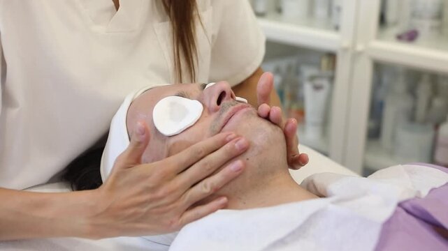 A person receives a facial treatment in a skincare clinic. A professional applies products and massages the face. The setting is bright and clean.