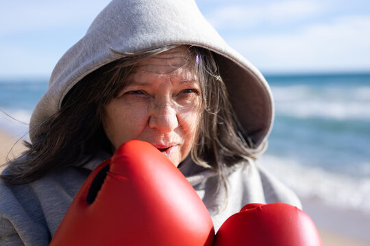 Senior woman with grey hair training boxing on beach with red gloves