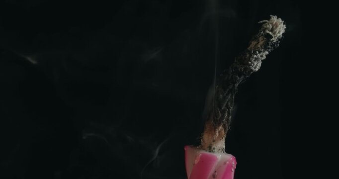 A candle is lit and has a pink and white striped wick