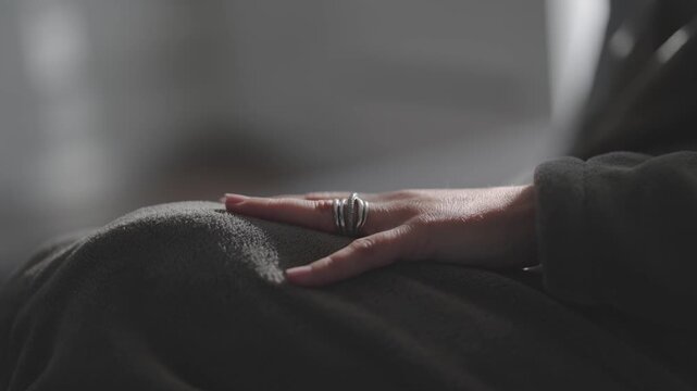 Anxious woman is sitting on a couch with her hand touching her lap. She is wearing a ring on her finger
