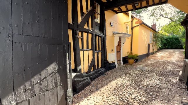 The side of an ancient house, from the 15th or 16th century, with a tall, covered, timber framed, entrance passage, for access by horse-drawn carriages, leading to a cobbled inner courtyard.