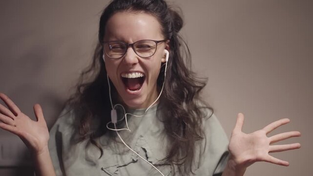 Dancing woman with curly long hair and glasses is smiling while wearing headphones, enjoying the music