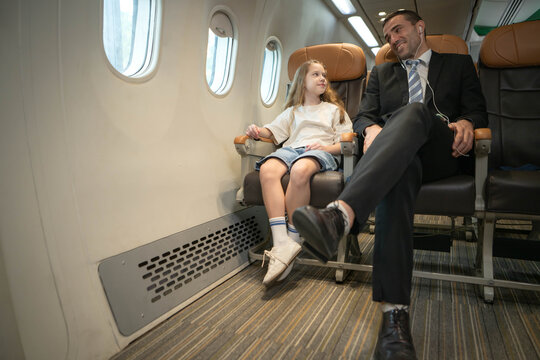 Businessman traveling with his daughter inside a commercial airplane cabin, representing family travel and business mobility