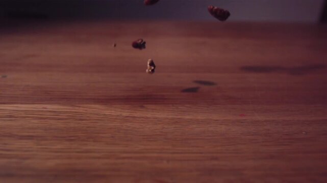 A cinematic close-up of coffee beans falling and scattering across a wooden surface, bathed in warm lighting.