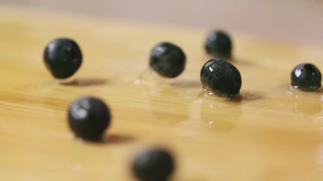 A cluster of fresh, dark blue-black blueberries scattered across a light brown wooden surface. 