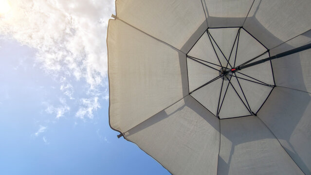 White umbrella providing shade under a bright blue sky with wispy clouds, symbolizing summer comfort, beach holidays, and relaxing outdoor leisure time