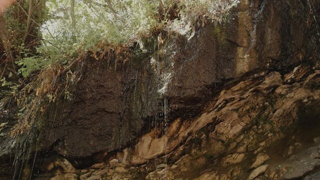 Still shot of thin water streams flowing over a damp rock wall inside a grotto.