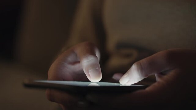A person is texting on a phone in the dark. Concept of isolation and loneliness, as the person is alone and focused on their phone. The darkness adds to the mood of the scene