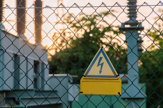 High voltage hazard warning sign on chain link fence at electrical substation during sunset, power grid safety and industrial security concept