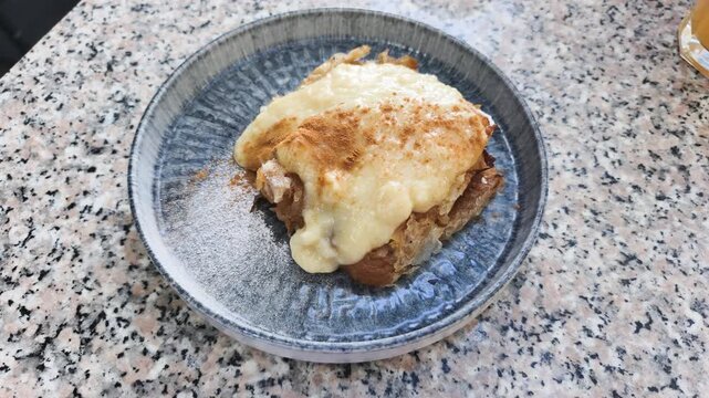 Cozy autumn dessert with traditional apple strudel sits on ceramic plate. Warm autumn dessert topped with sweet vanilla cream and cinnamon powder serves for delicious tea time in local cafe.