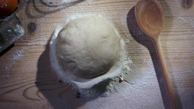 Ball of artisan bread dough falling onto a mound of flour on a rustic wooden table, capturing a warm, handcrafted baking atmosphere with natural textures and authentic bakery appeal.