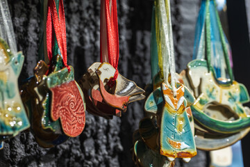 Fototapeta premium Colorful handmade ceramic Christmas ornaments, birds, mittens, foxes and angels hang from satin ribbons on a dark display backdrop, creating a festive, artisanal, seasonal and gift-shopping mood