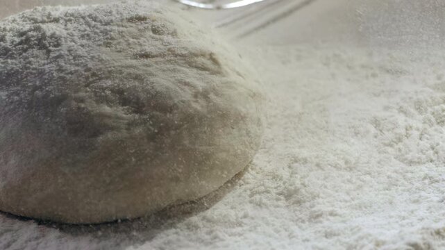 Raw bread dough ball dusted with flour as a cloud of fine flour falls over it at 1000 fps, creating a cinematic slow-motion baking scene with rich texture and artisanal appeal.