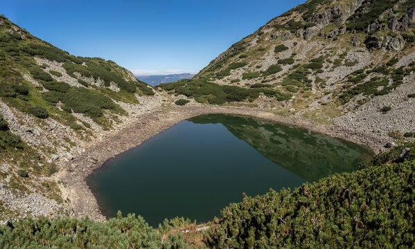 A scenic view of Mija Lake (Lacul Mija) nestled in a glacial cirque with rocky shores and alpine vegetation in the Par&acirc;ng Mountains, Romania.