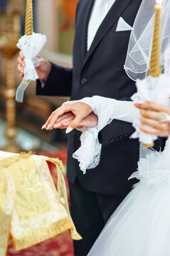 Bride and groom hold hands during a church wedding ceremony, surrounded by lit candles, lace veil details and formal attire, conveying love, unity and a sacred, romantic ritual.