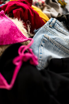 Messy pile of colorful laundry with a pink bra and denim shorts on a bedroom floor, casual garments in disarray