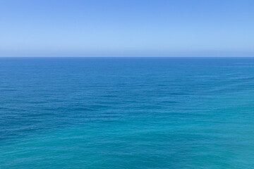 Fototapeta premium Minimalist view of the Atlantic Ocean meeting a clear blue sky in Nazare, Portugal, creating a seamless natural background with calm water and a distant horizon.