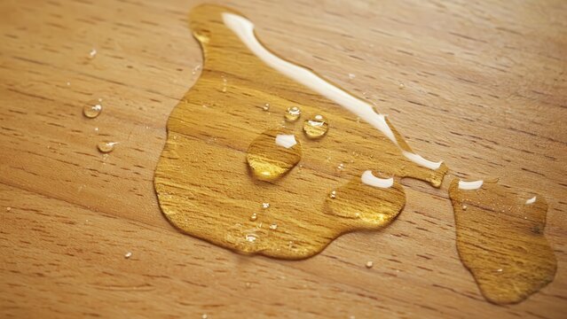 Honey puddle spreading across light wooden table