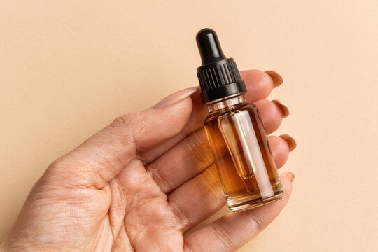 Dark amber glass bottle in female hand. Natural skin care SPA beauty product design. Mineral organic oil cosmetics on beige background. Mock-Up. Oily pipette. Face and body treatment. Blank logo label