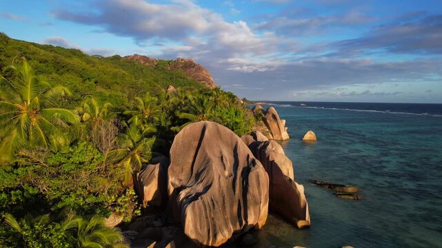 Anse Source d'Argent reveals granite boulders, palms and turquoise sea on La Digue in a smooth drone pull-back shot.