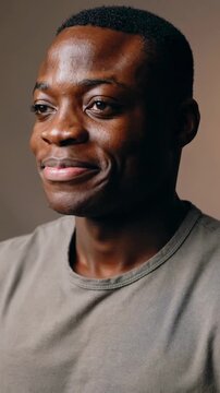 Vertical video: Receiving camera prompt, man revealing small smile in studio, wearing grey T-shirt